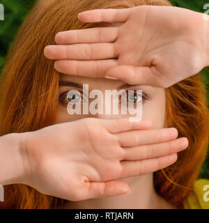 Beautiful young redhead woman hiding behind hands Stock Photo