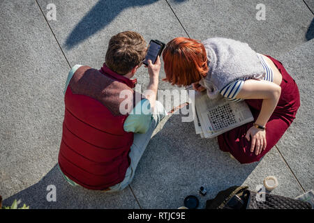 Young couple viewed from above sharing information about her crossword puzzle at Coal Drops Yard, Kings Cross, London, England Stock Photo