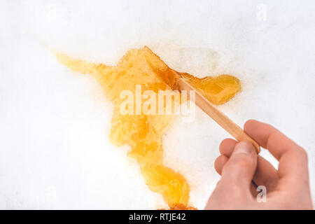 Sweet maple taffy on white snow. Hot maple taffy gets caramelized after being poured on cold snow. This traditional treat is popular in Quebec during  Stock Photo