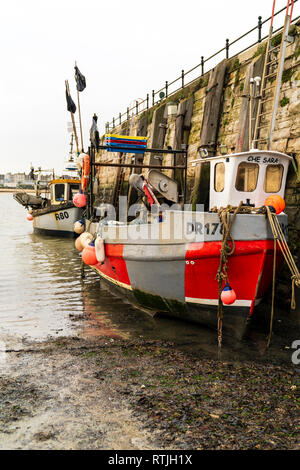 Two small single cabin fishing boats moored one behind the other against the stone wall of Margate harbour, front one half beached due to low tide. Stock Photo