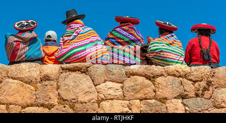 Peruvian Quechua indigenous people with traditional textiles, hats and hairstyles on an Inca wall in Chinchero, Cusco, Peru. Stock Photo