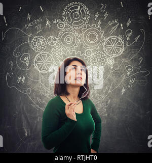 Smart woman meditate looking up thinking of new ideas in front of blackboard as gear cogwheels, arrows and mess drawn as thoughts around head. Concept Stock Photo