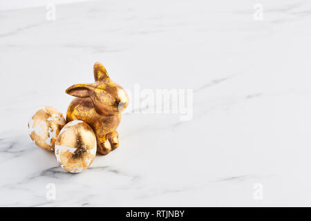 Easter greeting card, golden rabbit and eggs decorated with golden foil on white marble table with space for your greetings. Stock Photo