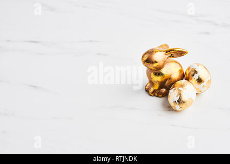 Easter greeting card, golden rabbit and eggs decorated with golden foil on white marble table with space for your greetings. Stock Photo