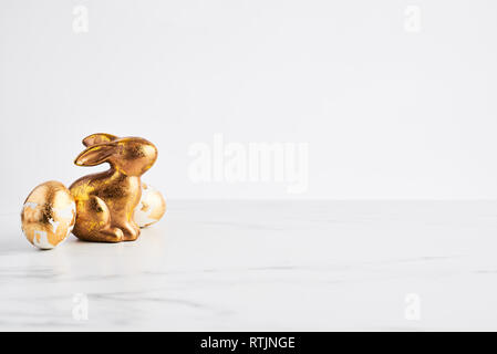 Easter greeting card, golden rabbit and eggs decorated with golden foil on white marble table over white background with space for your greetings. Stock Photo