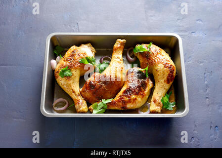 Baked chicken legs in baking tray on blue stone background.