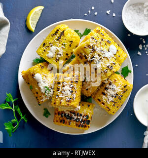 Grilled corn on the cob with sauce and parmesan over blue stone background. Top view, flat lay Stock Photo