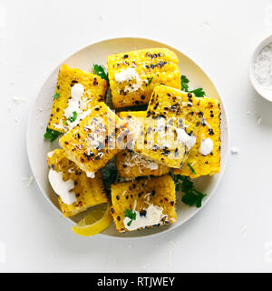 Grilled corn on cob with sauce and grated parmesan on plate over white stone background. Tasty vegetarian food. Top view, flat lay Stock Photo