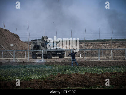 Gaza, Gaza strip, Gaza. 1st Mar, 2019. A young Palestinian demonstrator seen using a slingshot to hurl objects towards Israeli forces next to an armoured vehicle on the other side of the barbed-wire fence during the clashes with Israeli forces following a demonstration along the border with Israel east of Gaza City. Credit: Nidal Alwaheidi/SOPA Images/ZUMA Wire/Alamy Live News Stock Photo