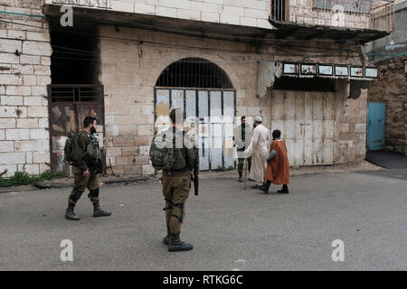 Israeli soldiers speaking to Palestinians walking through sealed Palestinian shops in Al-Shuhada Street which used to be the central wholesale market of the Hebron region and was closed to Palestinian merchants after violence in the Second Intifada in old city of Hebron West Bank Israel. Stock Photo