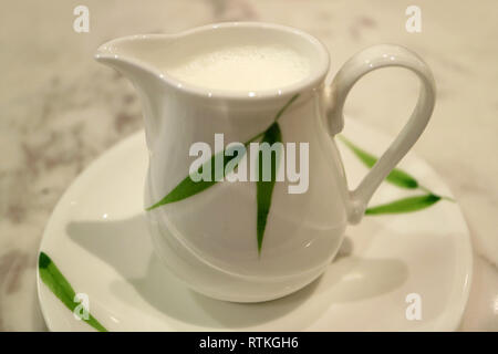 White with green leaf pattern milk pitcher on a saucer Stock Photo
