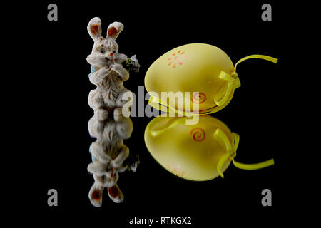 A yellow easter egg and ceramic bunny on black background Stock Photo