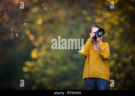 Pretty, female photographer taking pictures outdoor on a lovely autumn day - shallow DOF, color toned image