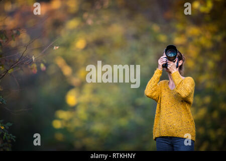 Pretty, female photographer taking pictures outdoor on a lovely autumn day - shallow DOF, color toned image