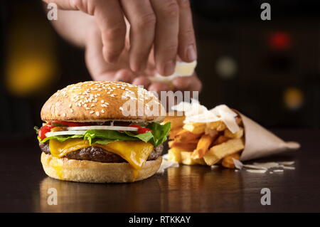 Hand that arranges beef burger with fried potatoes and cheese Stock Photo