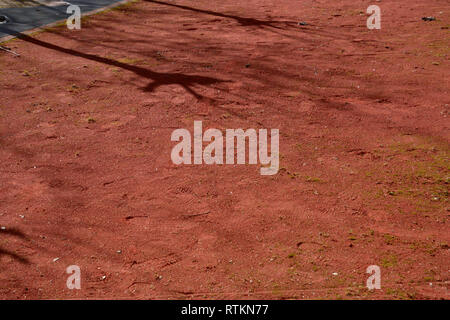 dirty traditional boules court made of red sand, soiled and unkempt bocce court in the spring with long shadows of trees and many footprints in the re Stock Photo