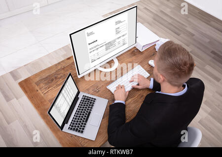 Happy Young Businessman Looking At Invoice On Computer Screen Near Laptop Stock Photo