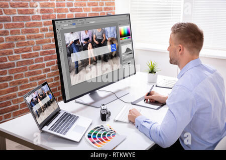 Male Designer's Hand Using Graphic Tablet While Working On Multiple Computers Stock Photo