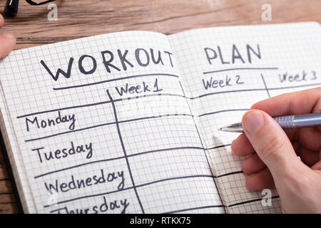Close-up Of A Person's Hand Writing Workout Plan In Checkered Pattern Notebook Stock Photo