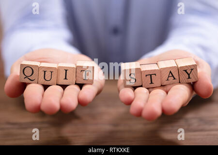 Close-up Businessman's Hand Holding Quit And Stay Blocks Over Wooden Desk Stock Photo