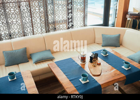 Spa hotel resort lounge zone with wooden table with blue napkins, teapot an mugs setting for tea party Stock Photo