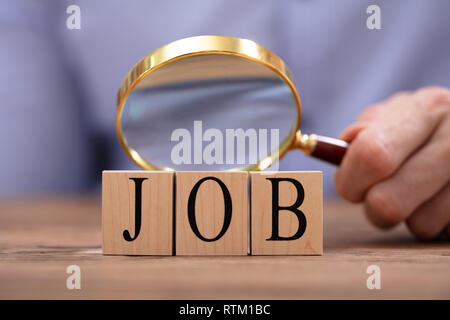 Close-up Of A Person's Hand Looking At Job Blocks Through Magnifying Glass On Desk Stock Photo