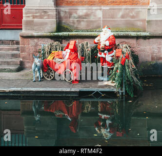 Statues of Santa Claus and his donkey with all the gifts near the Covered market of Colmar building with reflection in the Colmar Canal called Little Venice Stock Photo