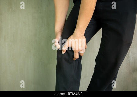 Man grab his knee experiencing pain isolated in grey background Stock Photo