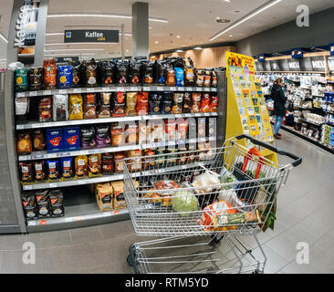 FRANKFURT, GERMANY - MAY 3, 2017: Shopping cart with vegetables next to a wide selection of coffee stand in a contemporary supermarket Stock Photo