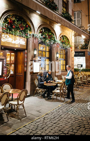 STRASBOURG, FRANCE - NOV 21, 2017: Le Pilier des Anges French restaurant on the iconic Rue Merciere with senior couple eating at the outdoor cafe paying the bill to the waiter Stock Photo