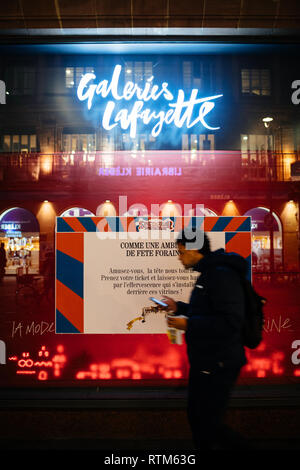 STRASBOURG, FRANCE - NOV 21, 2017: Man checking phone and eating while passing by Galeries Lafayette shop display in preparation for Christmas decoration Stock Photo