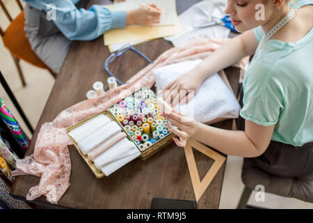 2 young beautiful female dressmakers cooperating in their own studio working as a team on new order. Small Business, partnership and friendship concep Stock Photo