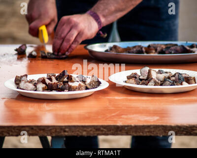 Unrecognizable person cutting meat with a knife and placing it on a paper plate in the street at a popular party in a village in Spain Stock Photo