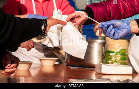 A person wearing blue nitrile gloves placing paper napkins, plastic forks and paper plates on a table during a street party Stock Photo