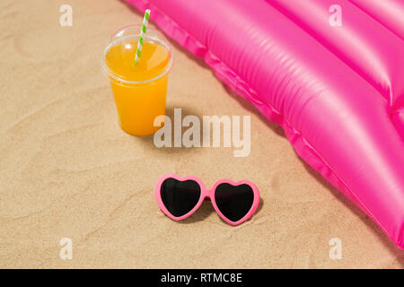 sunglasses, juice and pool mattress on beach sand Stock Photo
