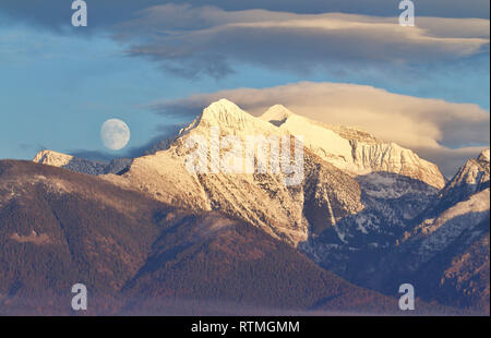 Moonrise over the snow capped peaks of the Mission Mountains in western Montana - the moon is 'real', NOT photoshopped into the scene Stock Photo