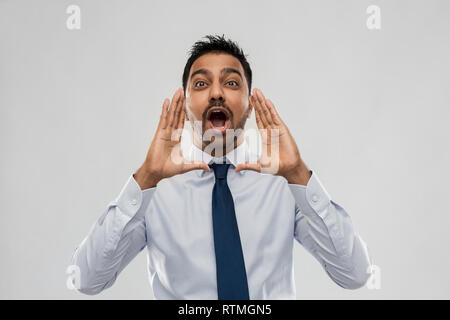 indian businessman shouting or calling over grey Stock Photo