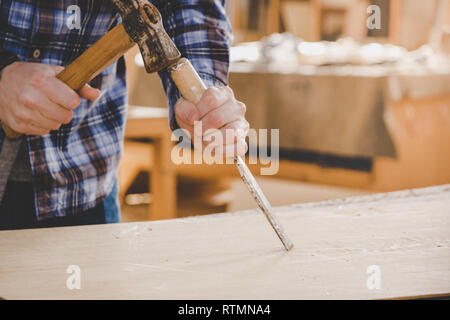 Carpenter working with chisel and hammer on wood. Workshop background. Carpenter workbench. Stock Photo
