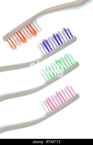 Vertical side view shot of four colorful toothbrushes with white handles isolated on white. Three are coming out from the left side while the other on Stock Photo