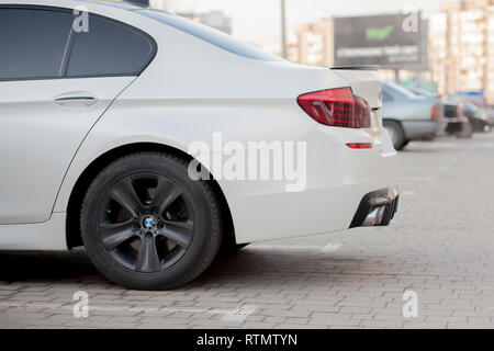 Kyiv, UKRAINE- February 27, 2019: Side view of white car parked in paved parking lot area on blurred suburb road background on bright sunny day. Trans Stock Photo