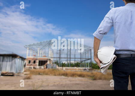 engineer holding white helmet standing and looking at construction site Stock Photo