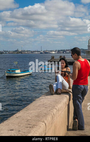 Havana, Cuba - 22 January 2013: A view of the streets of the city with cuban people. A couple relaxed on seawall malecon. Stock Photo