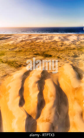 Backs of erodes sand dunes of Stockton beach in lead up to waterfront of Pacific ocean - aerial vertical panorama from ground surface to distant sky a Stock Photo