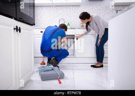 Woman Complaining Clog Sink To Young Male Plumber In Kitchen Stock Photo