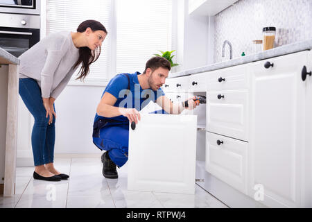 Woman Looking At Male Handyman Installing Cabinet Door In The Kitchen Stock Photo