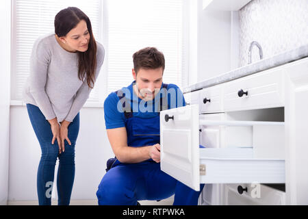 Woman Looking At Male Handyman Installing Door Of Drawer In The Kitchen Stock Photo