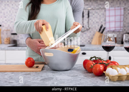 Mid-section Of Woman Grating Butter While Husband Hugging In Kitchen Stock Photo