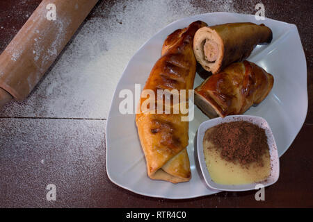 close up view of banana rolling, is a banana baked with sweet crepes roll and served with condensed milk and chocolate powder on a wooden table with w Stock Photo