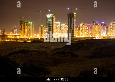 A beautiful shot of the city of Netanya in Israel during the night. bright city lights reflected off the water on a beach. Stock Photo