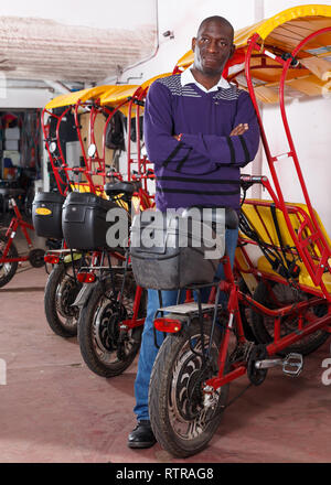 Joyful successful African American driver of pedicab offering touristic tour Stock Photo